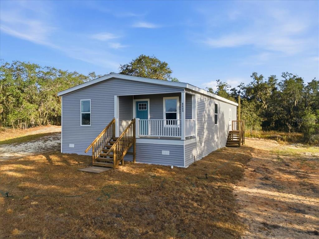 A gray manufactured home features a front porch with wooden stairs and a blue door — 449 STONE STREET, WILDWOOD, FL