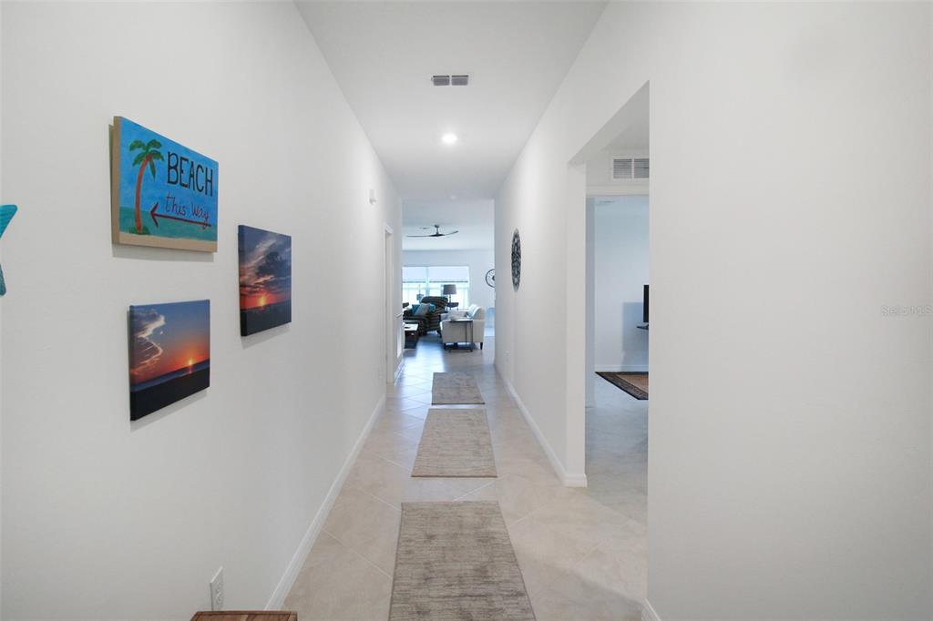 A bright hallway with tile flooring leads toward an open living area with wall art — 1346 FIRESIDE STREET, PORT CHARLOTTE, FL