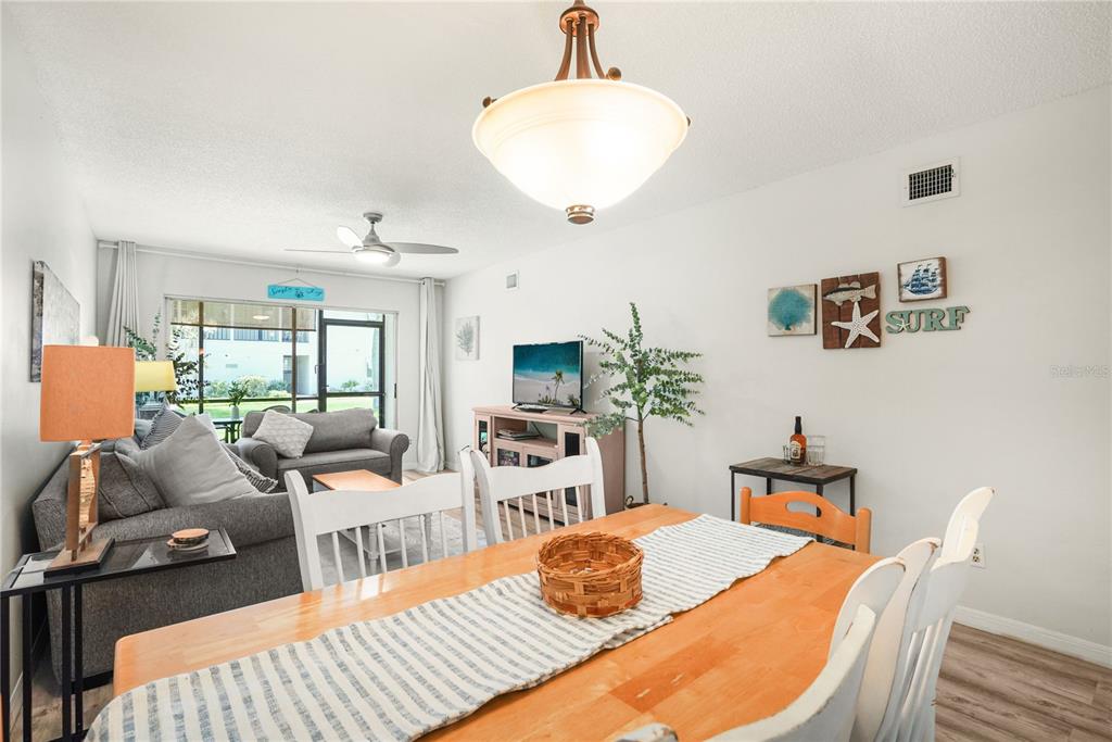 A dining area with a wooden table leads into a living room with gray furniture — 5673 MIDNIGHT PASS ROAD UNIT 201, SARASOTA, FL
