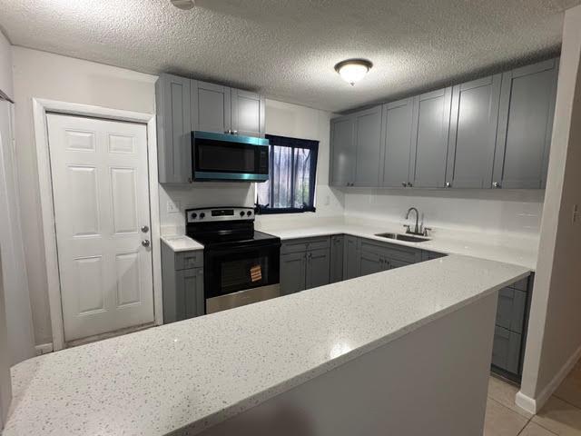 A kitchen features gray cabinets, white countertops, a microwave, and a stainless steel stove — 322 SW 2nd Street # 3, Pompano Beach FL 33060, POMPANO BEACH, FL