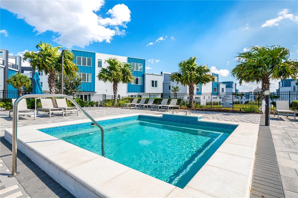 A rectangular swimming pool with a metal handrail sits on a paved patio with palm trees — 7740 SANDY RIDGE DRIVE UNIT 230, KISSIMMEE, FL