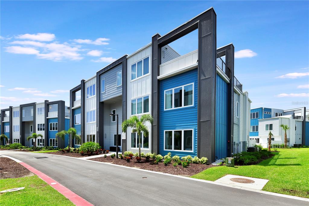A modern three-story apartment building features blue and white siding with dark gray structural framing — 7740 SANDY RIDGE DRIVE UNIT 230, KISSIMMEE, FL
