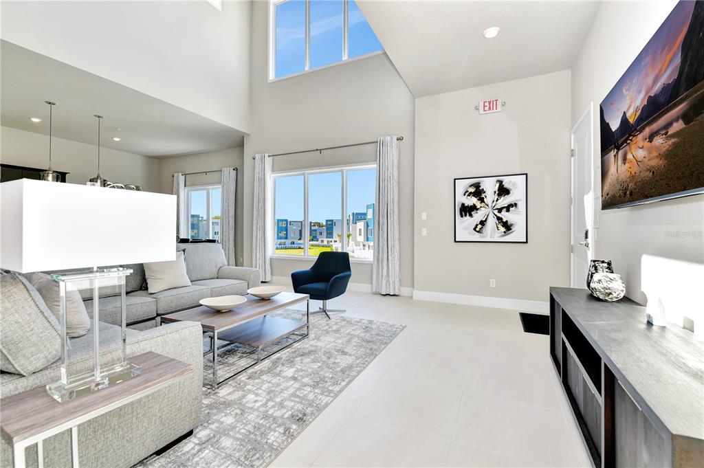A modern living room features high ceilings, large windows, a gray sofa, and tile flooring — 7740 SANDY RIDGE DRIVE UNIT 230, KISSIMMEE, FL