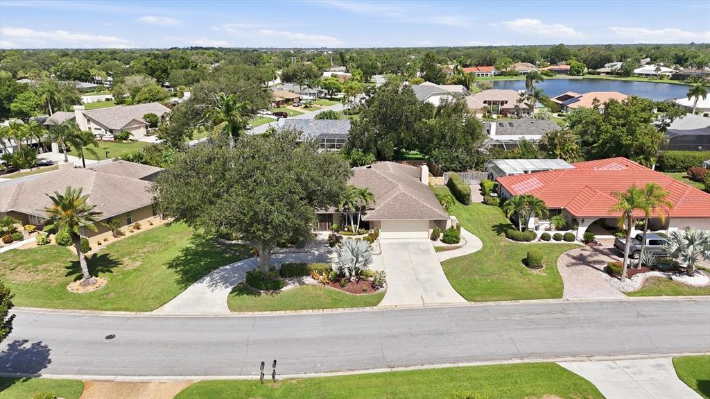 An aerial view shows a suburban street with several single-story houses and a nearby lake — 5511 COUNTRY LAKES TRAIL, SARASOTA, FL