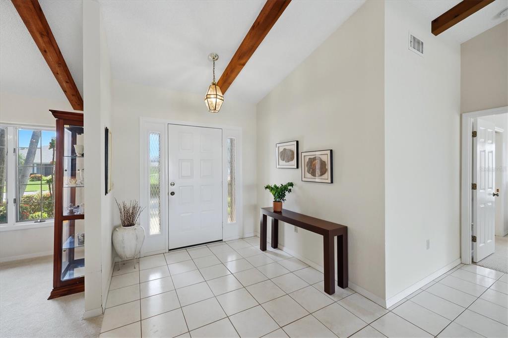 A bright entryway features white tile floors, a vaulted ceiling with wood beams, and a console — 5511 COUNTRY LAKES TRAIL, SARASOTA, FL
