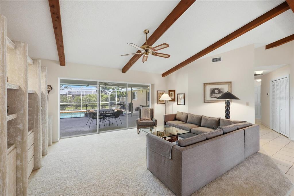 A living room features vaulted ceilings with exposed wood beams, carpeted flooring, and sliding glass doors — 5511 COUNTRY LAKES TRAIL, SARASOTA, FL
