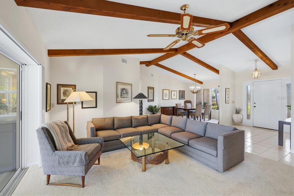 A living room with vaulted ceilings, exposed wooden beams, a sectional sofa, and dining area — 5511 COUNTRY LAKES TRAIL, SARASOTA, FL