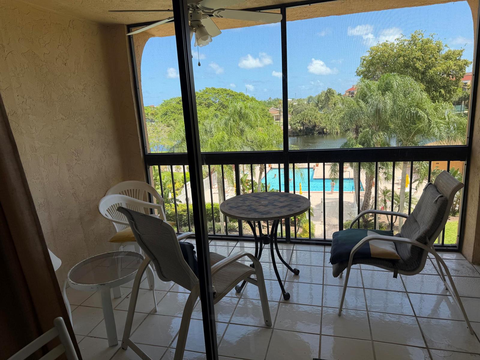 A screened-in balcony with tile flooring overlooks a swimming pool, pond, and palm trees — 2255 Lindell Boulevard # 4406, Delray Beach FL 33444, DELRAY BEACH, FL