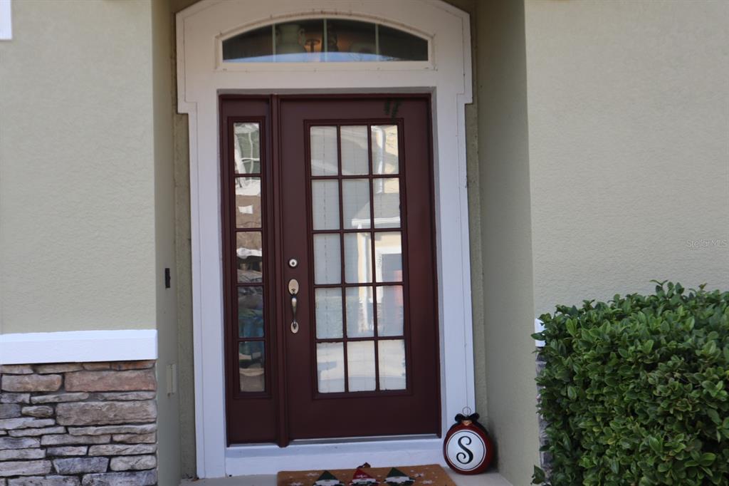 A dark red front door with glass panes and a sidelight sits in a white frame — 3026 VICTORIA GLEN DRIVE, SANFORD, FL