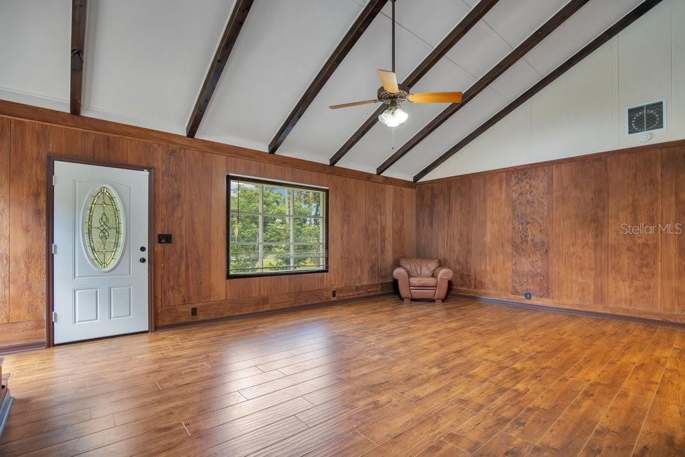 A living room features wood-paneled walls, vaulted ceilings with exposed beams, and wood-look flooring — 110 W WASHINGTON AVENUE, DELAND, FL