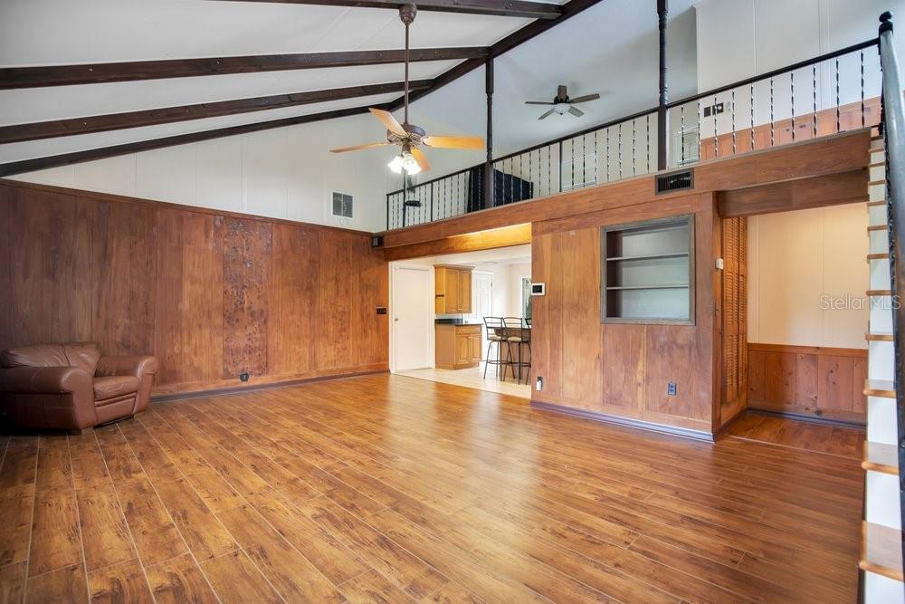 A living room with wood-paneled walls, vaulted ceilings, a loft area, and wood-look flooring — 110 W WASHINGTON AVENUE, DELAND, FL