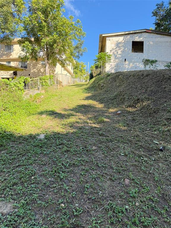 A grassy, sloped path sits between a two-story house and an unfinished concrete structure — CAFARNAUM SOLAR 118, AIBONITO, PR