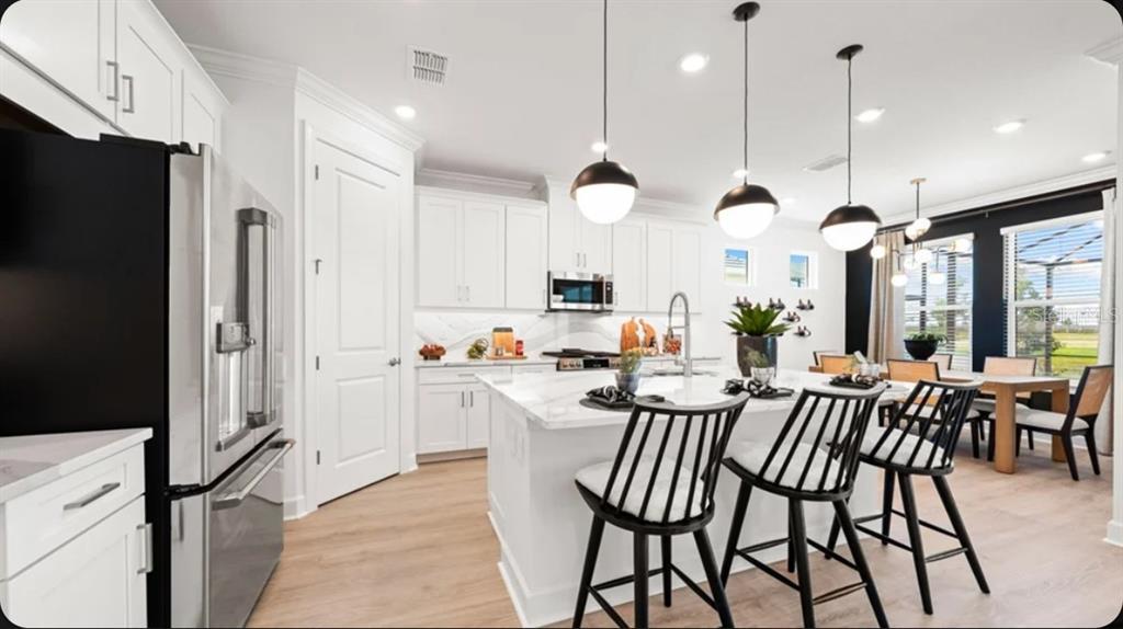 A modern white kitchen features a large marble island with black stools and pendant lighting — 7416 MOONBEAM AVENUE, SARASOTA, FL