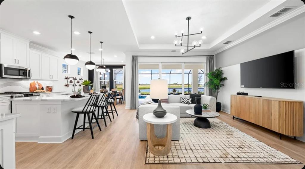 An open-concept living room and kitchen featuring white cabinetry, wood flooring, and a pool view — 7416 MOONBEAM AVENUE, SARASOTA, FL