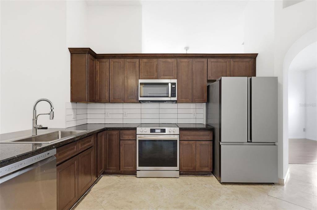 A kitchen features dark wood cabinets, stainless steel appliances, black countertops, and white subway tile — 13714 HUNTWICK DRIVE, ORLANDO, FL