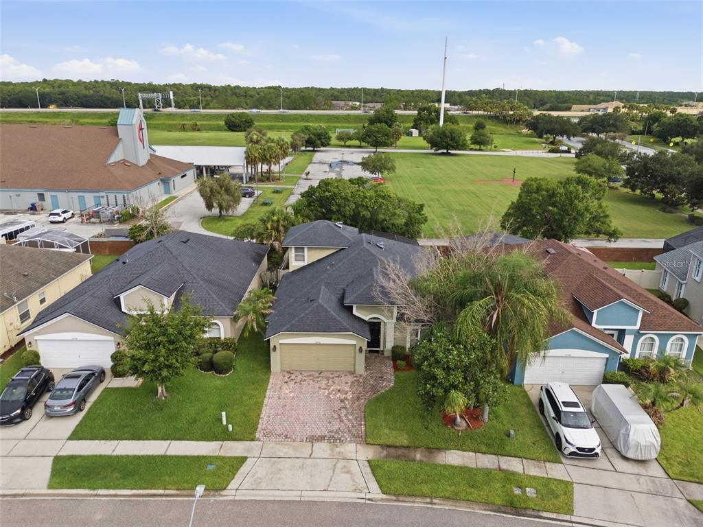 An aerial view shows three suburban houses with driveways and lawns near a large grassy field — 13714 HUNTWICK DRIVE, ORLANDO, FL