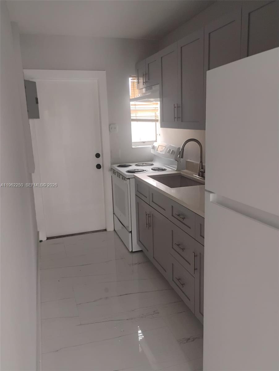 A small kitchen features gray cabinets, white appliances, and light-colored tile flooring — 908 SW Avenue D, Belle Glade FL 33430, BELLE GLADE, FL