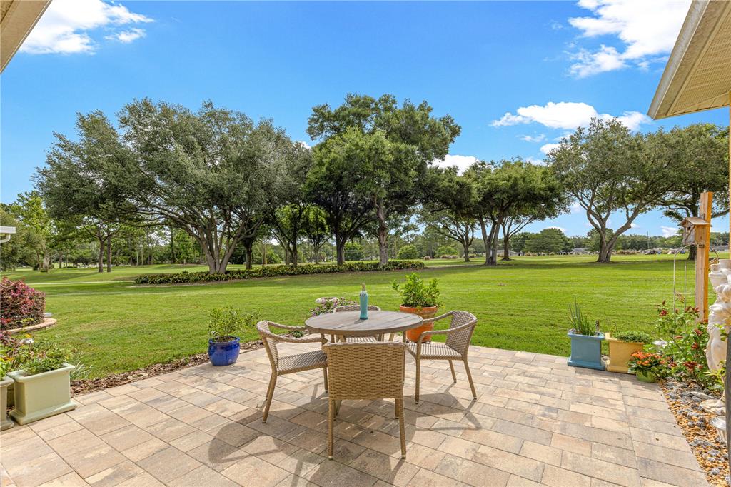 A paved patio features a small dining set overlooking a large grassy yard with trees — 9359 SW 94TH LOOP, OCALA, FL