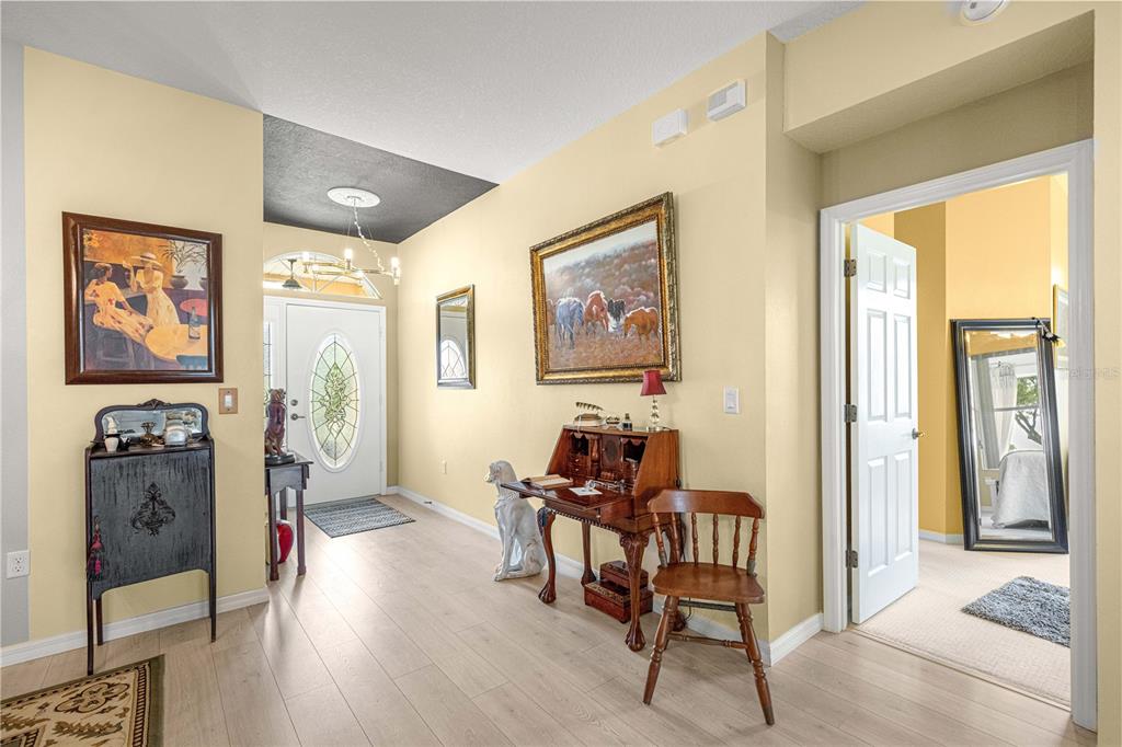 An entryway features light wood flooring, yellow walls, a wooden desk, and a front door — 9359 SW 94TH LOOP, OCALA, FL