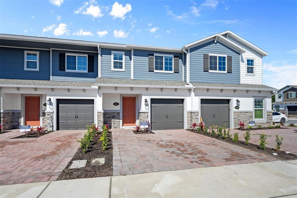 A row of three modern townhouses features blue siding, stone accents, and paved driveways — 4410 CAMPSITE LOOP, ORLANDO, FL