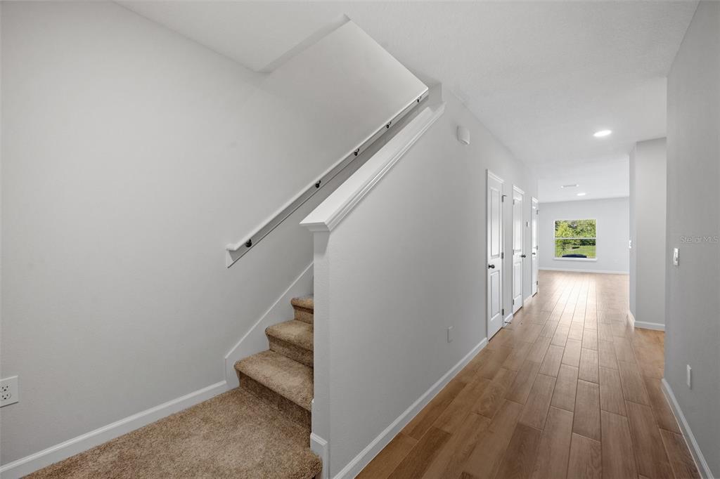 A hallway with wood-look tile flooring leads to a window, with carpeted stairs on the left — 4410 CAMPSITE LOOP, ORLANDO, FL
