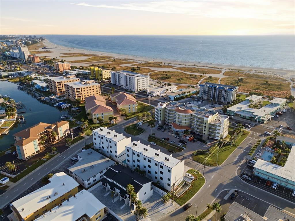 An aerial view shows a coastal neighborhood with multi-story apartment buildings, a canal, and beach — 11605 1ST STREET E UNIT A2, TREASURE ISLAND, FL