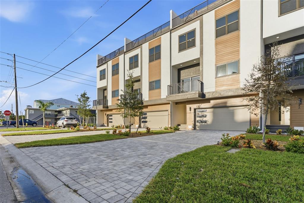 A row of modern three-story townhomes with paved driveways and attached garages under a blue sky — 11605 1ST STREET E UNIT A2, TREASURE ISLAND, FL