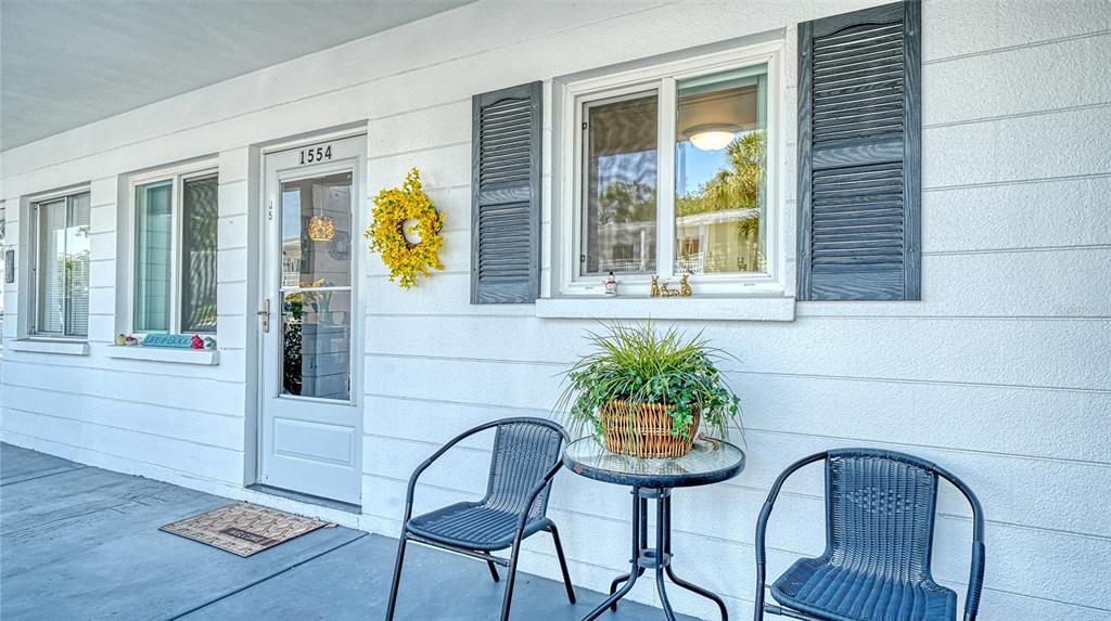 A white exterior wall features a front door, two windows with shutters, and patio furniture — 1554 PLEASANT ROAD UNIT J5, BRADENTON, FL