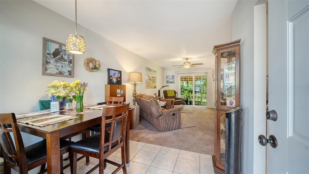 A dining area with a wooden table transitions into a carpeted living room with sliding doors — 1554 PLEASANT ROAD UNIT J5, BRADENTON, FL