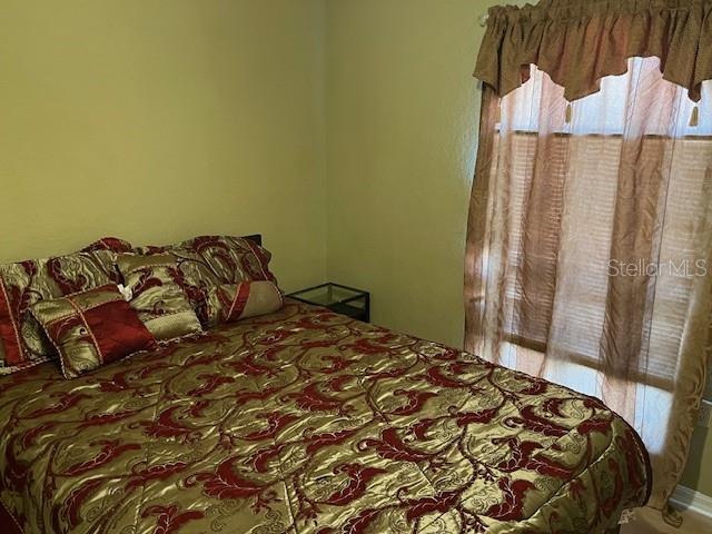 A bedroom features a bed with a gold and red patterned comforter and sheer curtains — 3723 IMPERIAL DRIVE, WINTER HAVEN, FL