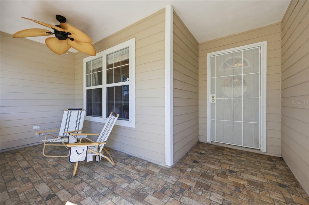 A covered porch features tan siding, a ceiling fan, stone-look flooring, and two folding chairs — 347 ASHLEY STREET, HAWTHORNE, FL