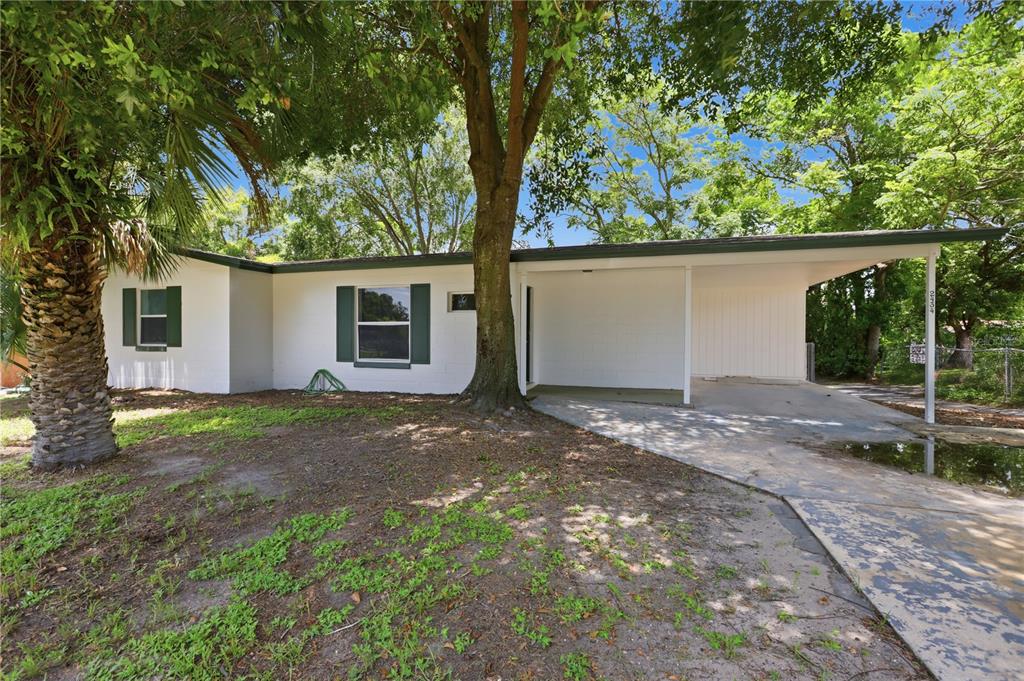 A single-story white house with a carport, dark shutters, and a large tree in front — 2434 CARDENA AVENUE, DELTONA, FL