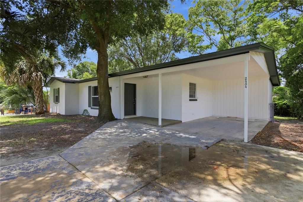 A single-story white house with a carport and a large tree in the front yard — 2434 CARDENA AVENUE, DELTONA, FL