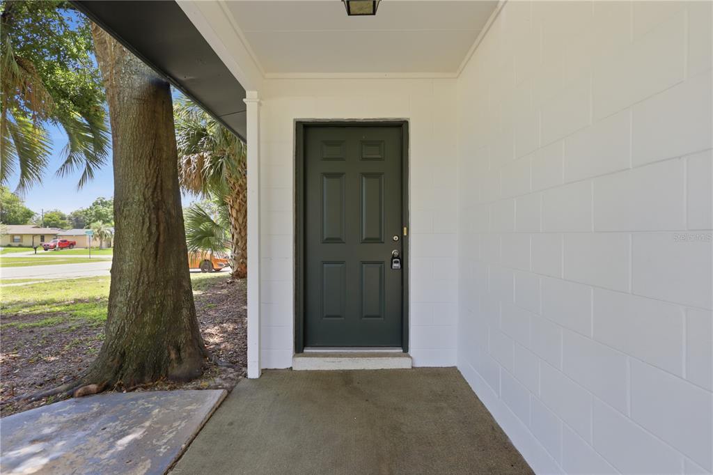A dark green front door is set into a white concrete block wall under a porch — 2434 CARDENA AVENUE, DELTONA, FL