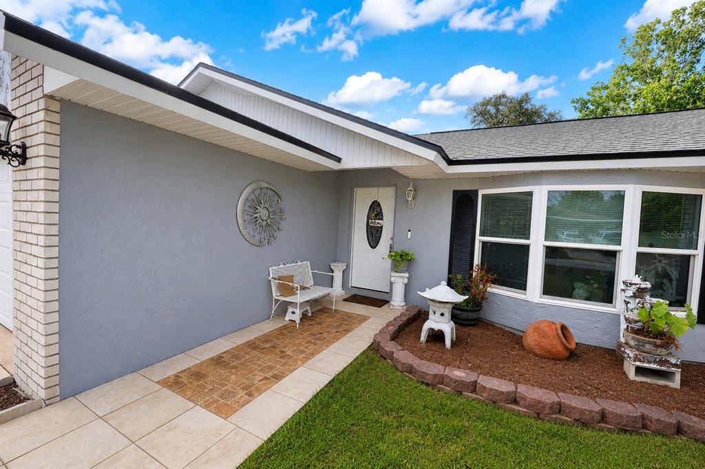 A gray house exterior features a white front door, a tiled porch, and landscaping — 1822 S HOUSTON DR, DELTONA, FL