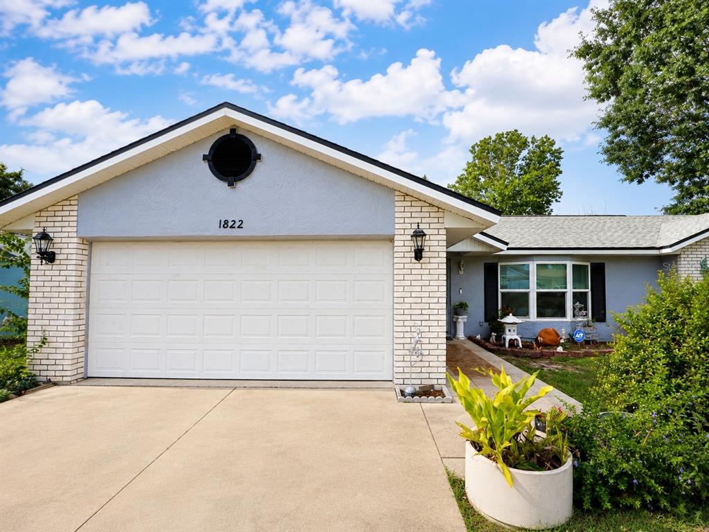 A single-story house with a white brick facade, a two-car garage, and a bay window — 1822 S HOUSTON DR, DELTONA, FL