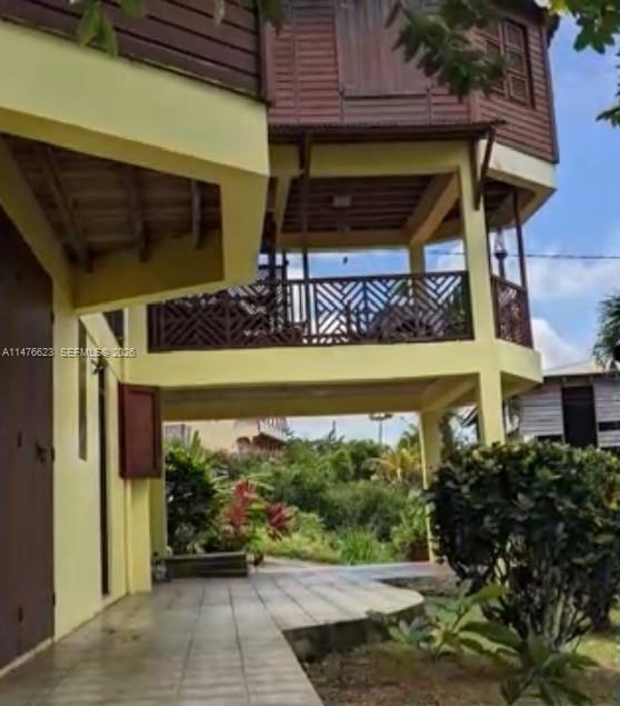 A two-story house with a yellow exterior, a raised wooden upper level, and a tiled patio — 0 CALIBISHE, DOMINICA, 00000, FL