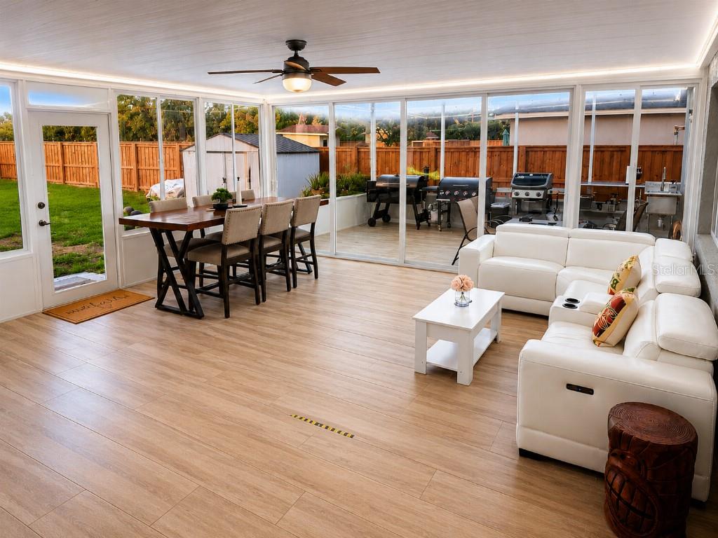 A sunroom with wood-look flooring, a dining set, a white sectional sofa, and glass walls — 1660 GLADIOLAS DRIVE, WINTER PARK, FL