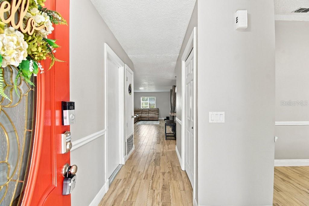 A hallway with light wood-look flooring leads from a red front door to a living area — 1660 GLADIOLAS DRIVE, WINTER PARK, FL