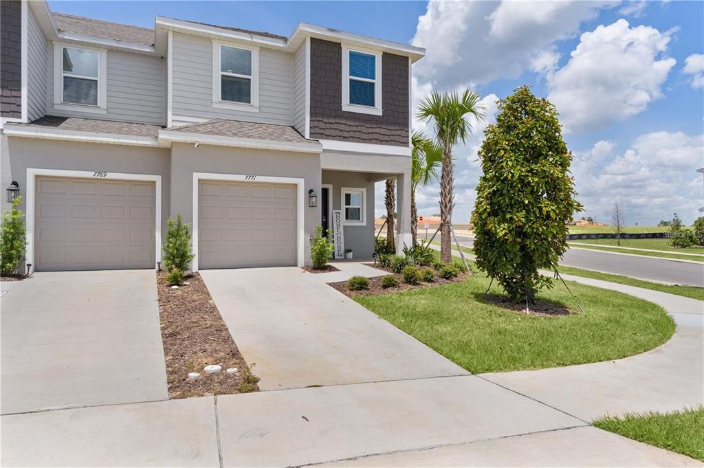 A two-story townhouse exterior features a beige facade, two garage doors, and a small lawn — 7771 WATERSCAPE, GROVELAND, FL