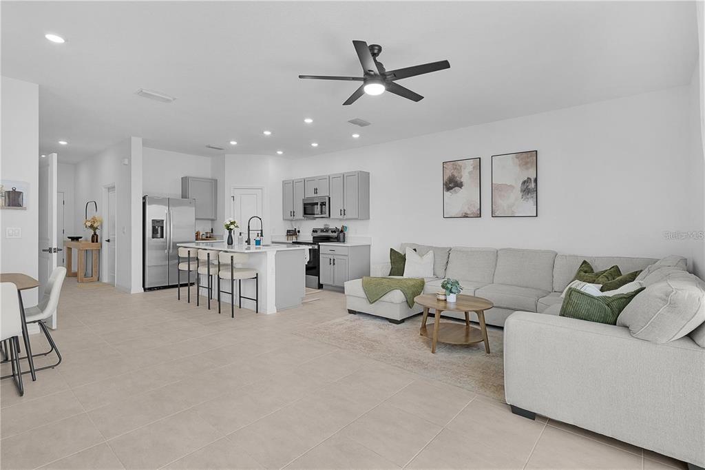 An open-concept living room and kitchen with light tile floors, grey cabinetry, and a sectional — 7771 WATERSCAPE, GROVELAND, FL