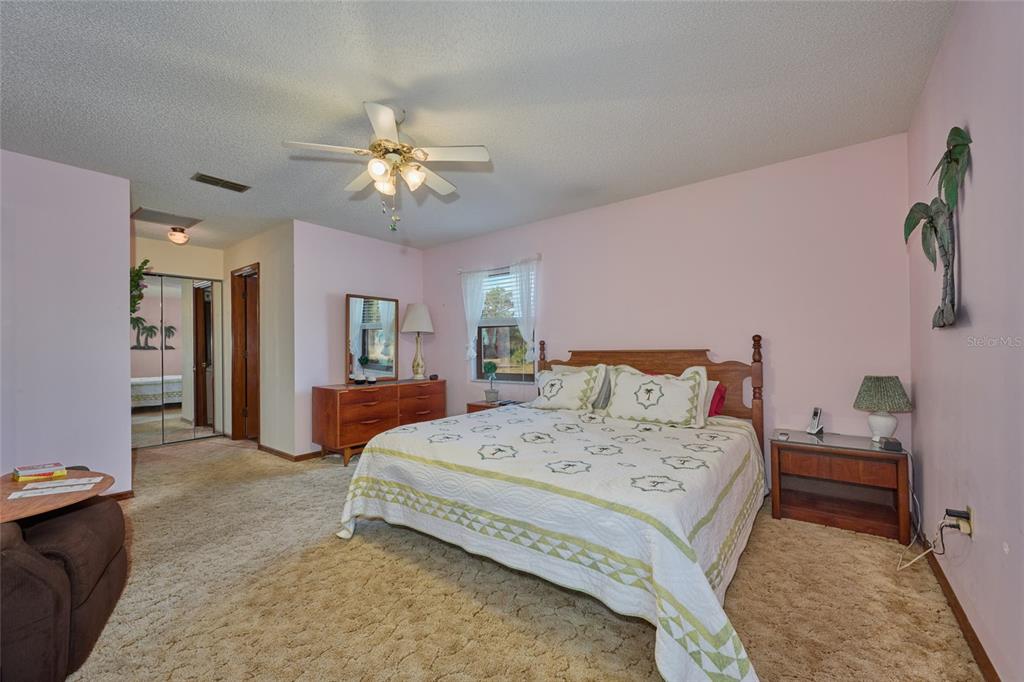 A bedroom features pink walls, beige carpeting, a ceiling fan, and a wooden bed frame — 4220 OLEANDER DRIVE, INDIAN LAKE ESTATES, FL