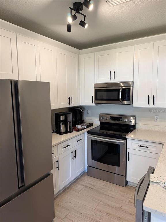 A kitchen features white cabinets, stainless steel appliances, and light wood-look flooring — 1532 BLUE MAGNOLIA ROAD, BRANDON, FL