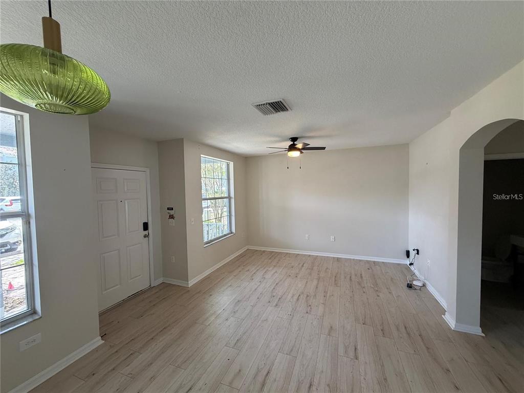 An empty living room features light wood-look flooring, a ceiling fan, and a green pendant light — 1532 BLUE MAGNOLIA ROAD, BRANDON, FL