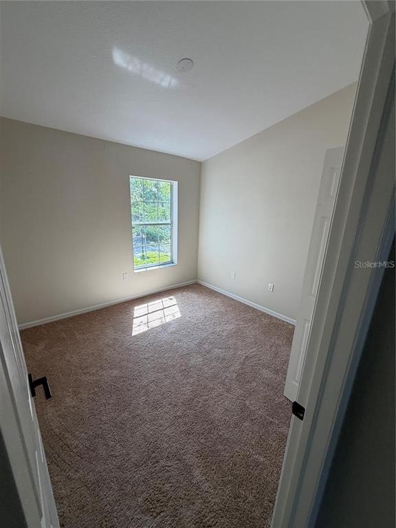 An empty bedroom features beige walls, tan carpeting, and a single window — 1532 BLUE MAGNOLIA ROAD, BRANDON, FL