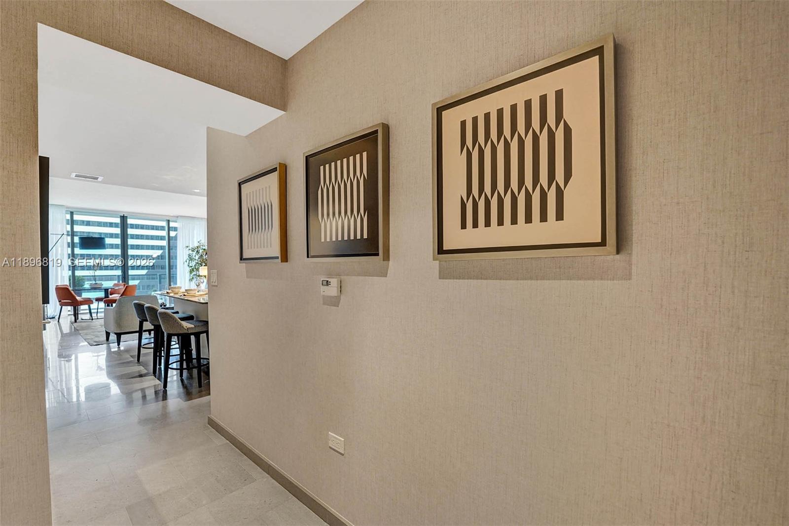 A hallway with three framed geometric prints leads to an open-plan kitchen and living area — 88 SW 7th St # 1408, Miami FL 33130, MIAMI, FL