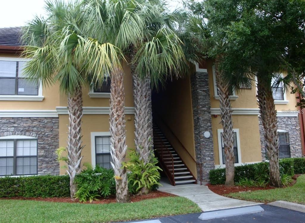 A two-story apartment building exterior features tan stucco, stone accents, palm trees, and stairs — 2209 PORTOFINO PLACE UNIT 2516, PALM HARBOR, FL