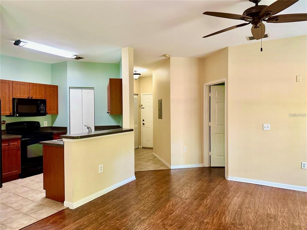 An open-concept kitchen with wood cabinets and dark appliances overlooks a living area with flooring — 2209 PORTOFINO PLACE UNIT 2516, PALM HARBOR, FL