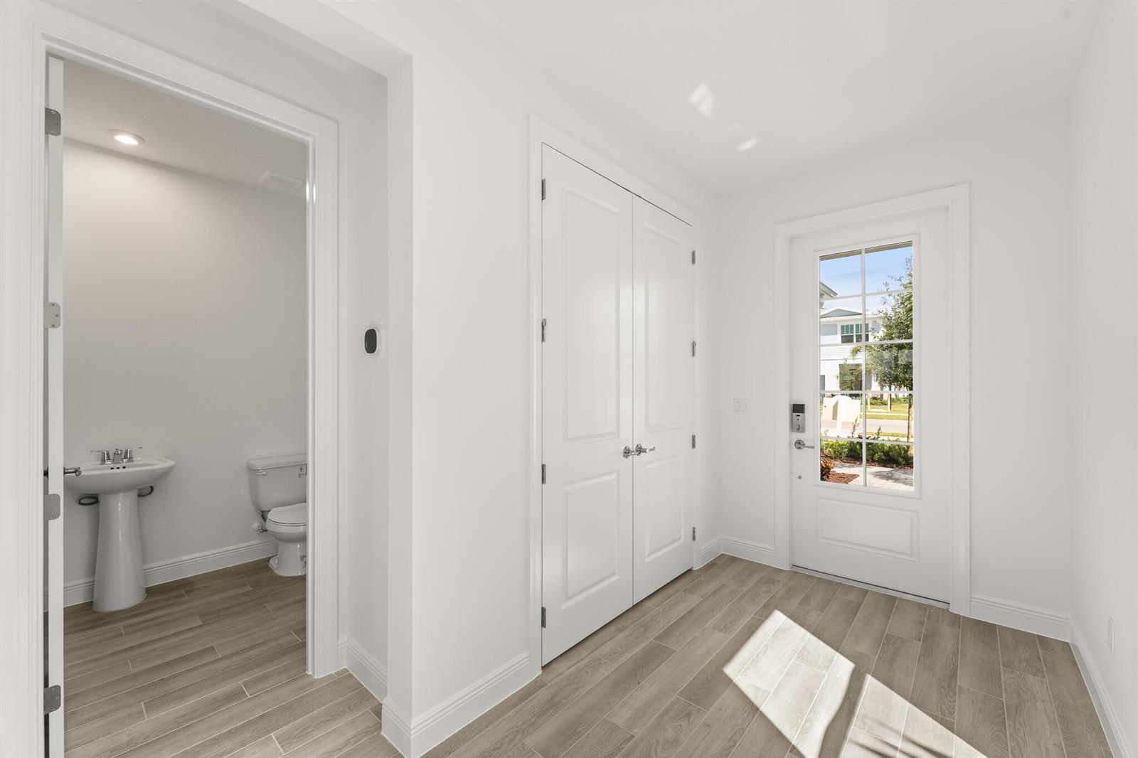 A bright entryway features wood-look tile flooring, a double-door closet, and an adjacent powder room — 1439 NW Corteal Way, Jensen Beach FL 34957, JENSEN BEACH, FL
