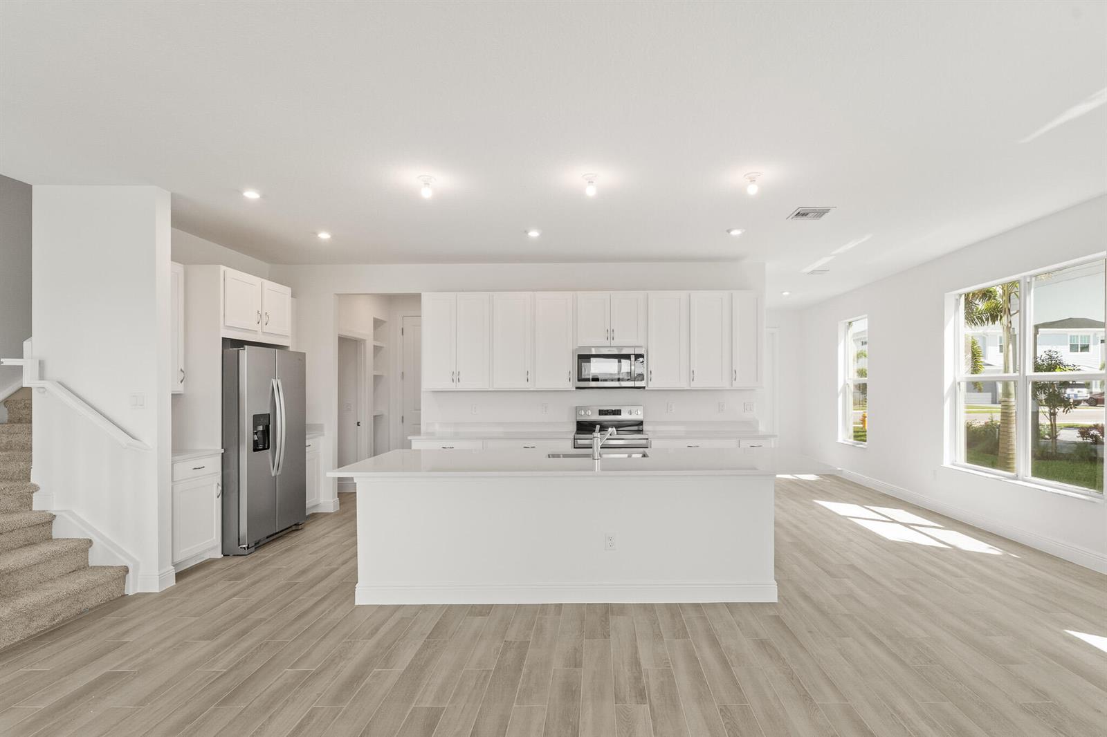 A modern kitchen features white cabinetry, stainless steel appliances, a central island, and wood-look flooring — 1439 NW Corteal Way, Jensen Beach FL 34957, JENSEN BEACH, FL